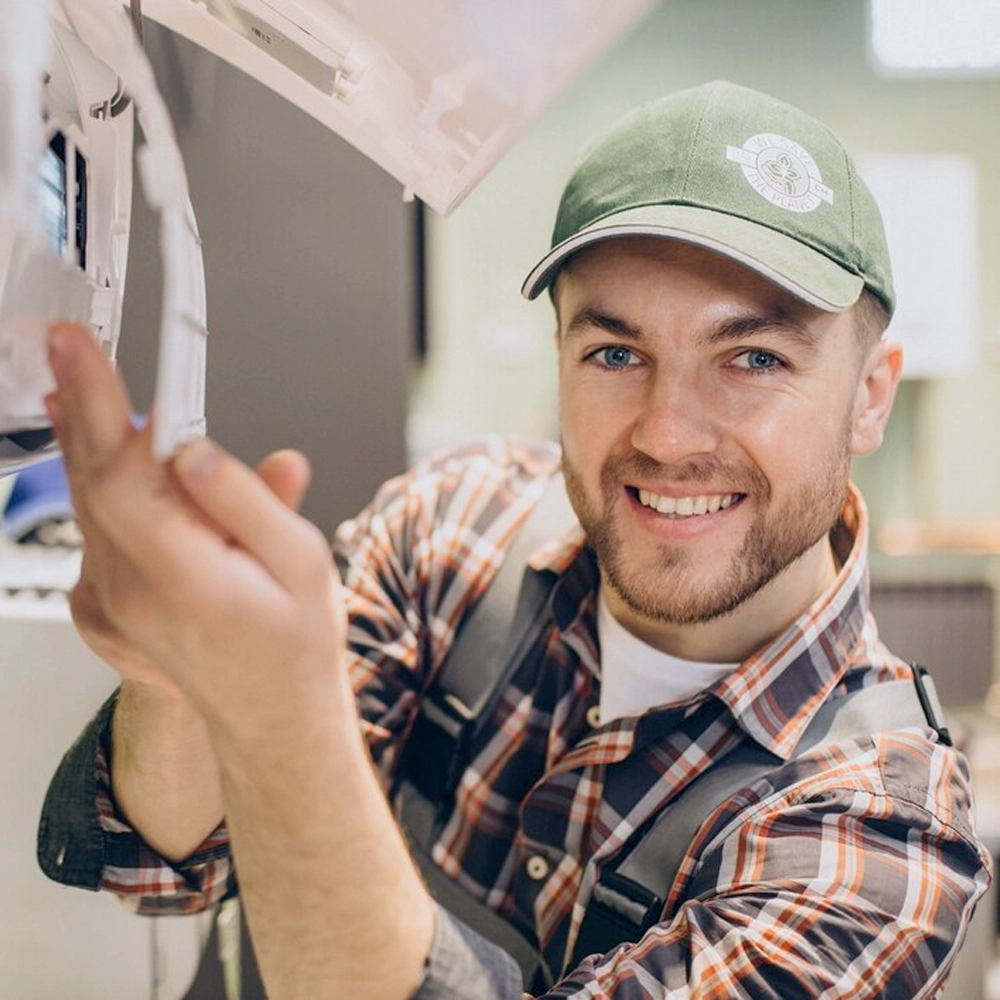 Smiling HVAC technician in a cap, inspecting an indoor air conditioning unit and checking its components