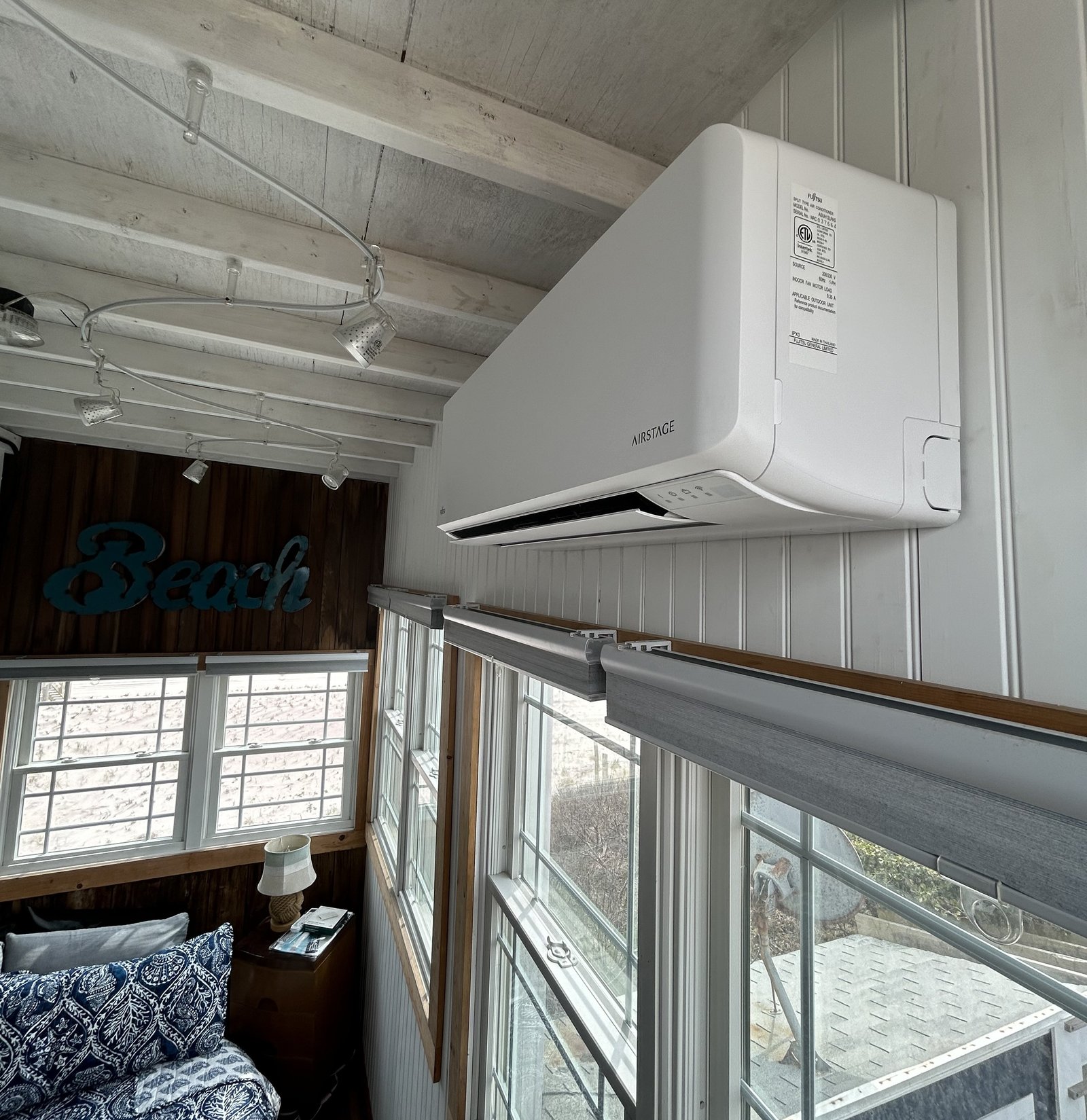 Airstage mini-split indoor unit installed in a coastal-style bedroom with exposed wooden beams and large windows overlooking an outdoor area.