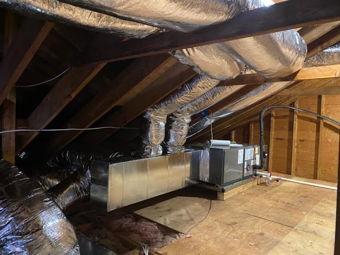 HVAC air handler unit installed in an attic with insulated flexible ductwork and metal ducting for air distribution.