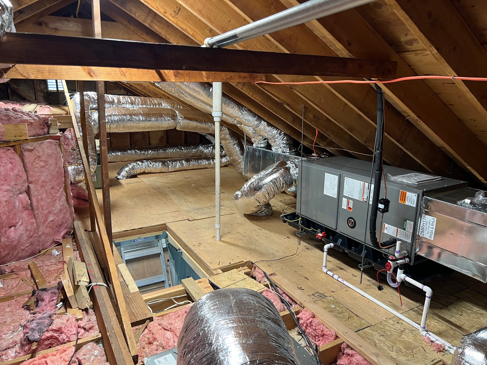 Outdoor installation of a Fujitsu mini-split unit alongside a central air conditioning condenser on the exterior of a house with beige vinyl siding