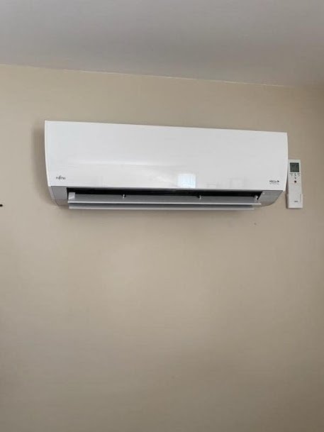 Fujitsu mini-split indoor unit mounted on a beige wall with a remote control installed beside it.