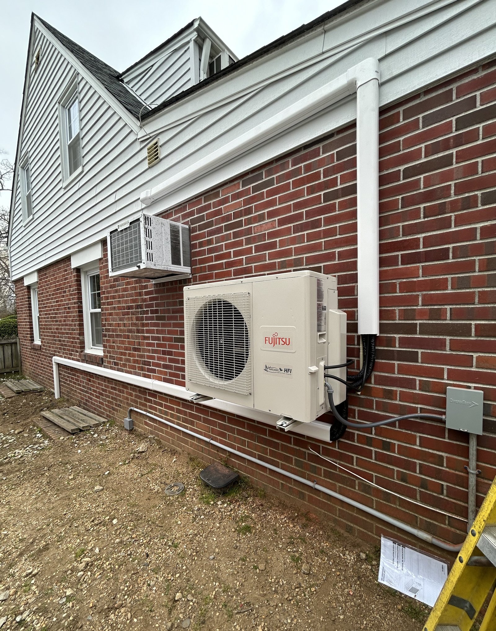 Fujitsu mini-split HVAC system installed on the exterior brick wall of a house, with insulated refrigerant lines and electrical conduit neatly secured along the wall.