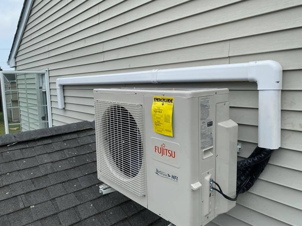 Fujitsu mini-split outdoor unit installed on a shingled roof against a house with vinyl siding, with protective conduit for refrigerant lines.
