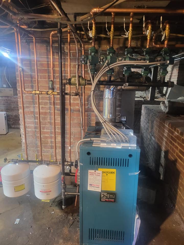 Hydronic boiler system installed in a brick-walled basement with multiple circulator pumps, copper piping, and expansion tanks.