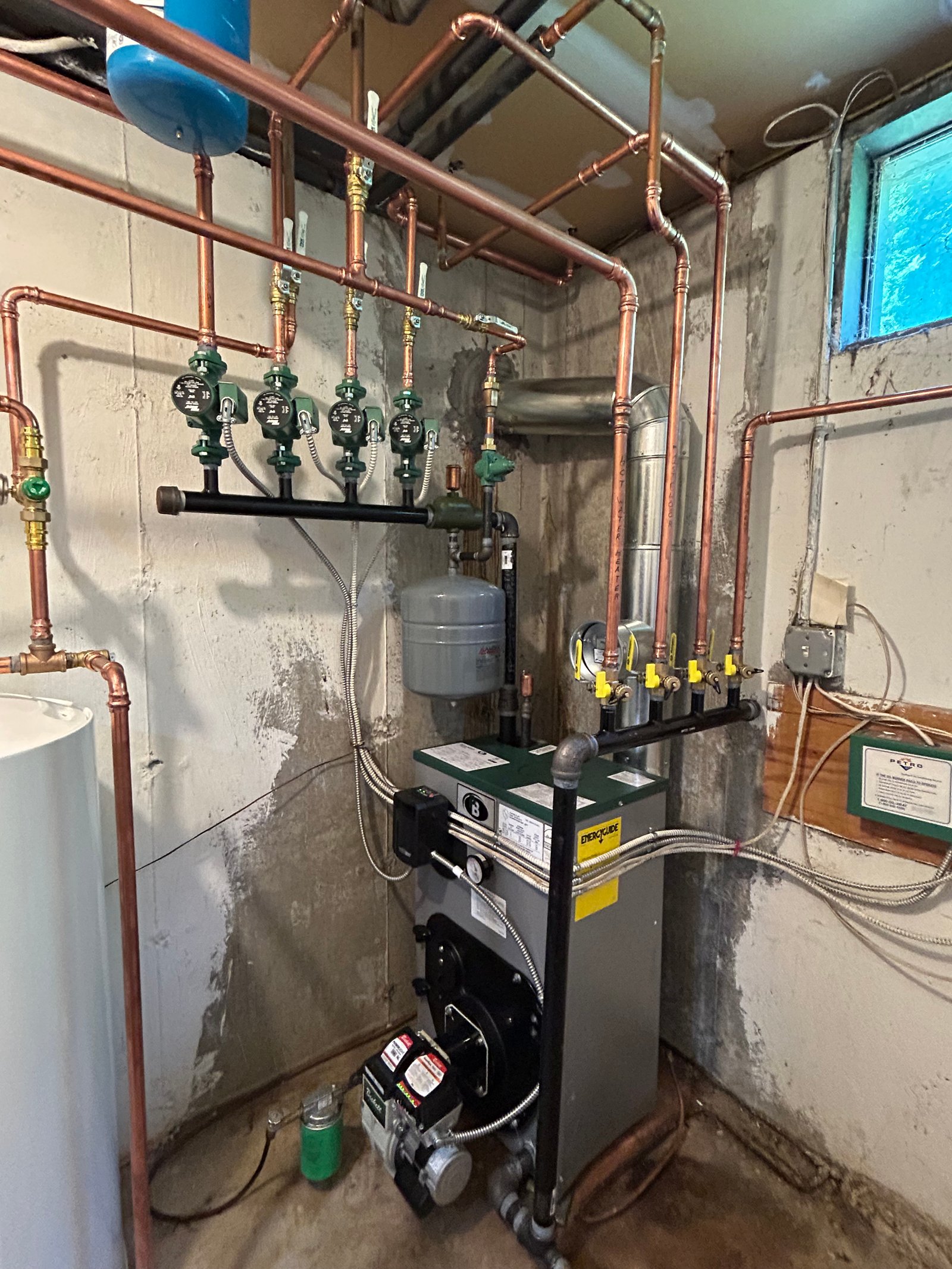 Oil-fired boiler heating system installed in a basement with copper piping, multiple circulator pumps, an expansion tank, and a venting system.