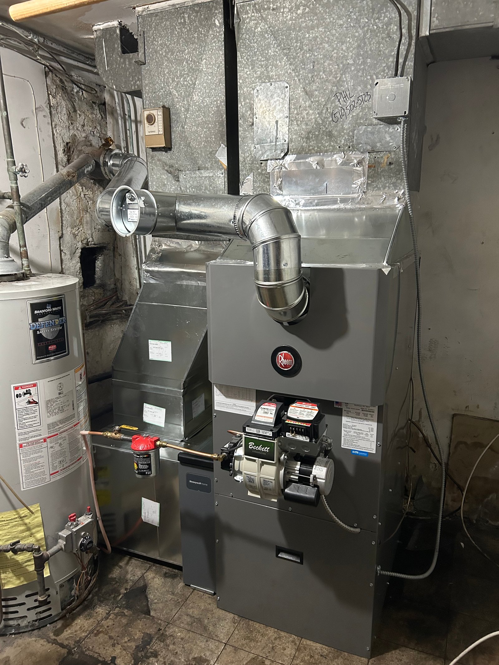 Rheem oil furnace installed in a basement with galvanized ductwork, an exhaust vent pipe, and a nearby water heater, showcasing a complete HVAC heating system setup.